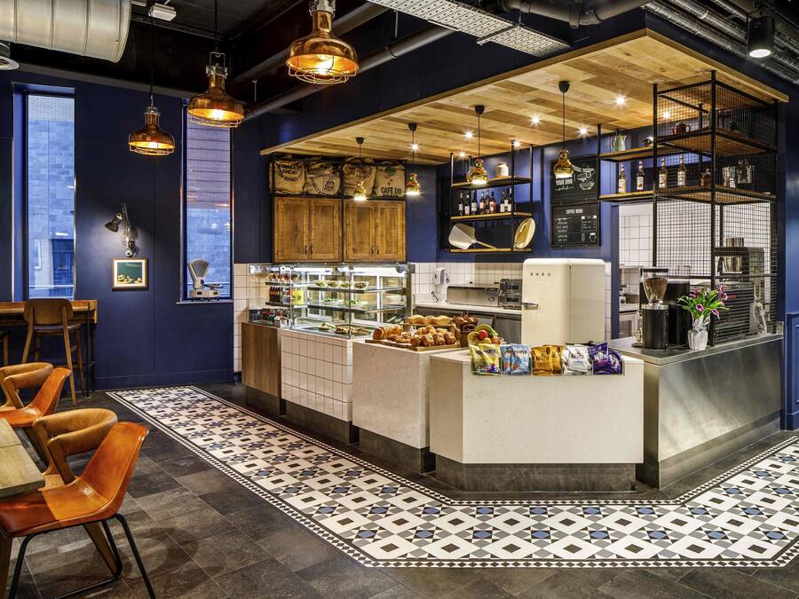 A modern cafe with a central counter, seating area, and a coffee menu board.
