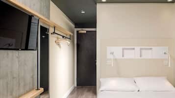 A modern hotel room with a wooden shelf, a bed with white linens, a mounted TV, and a wall-mounted power outlet.