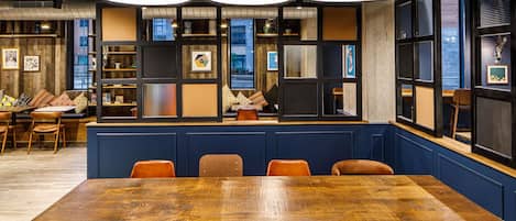 Un comedor moderno con una gran mesa de madera, sillas color naranja e iluminación colgante negra.