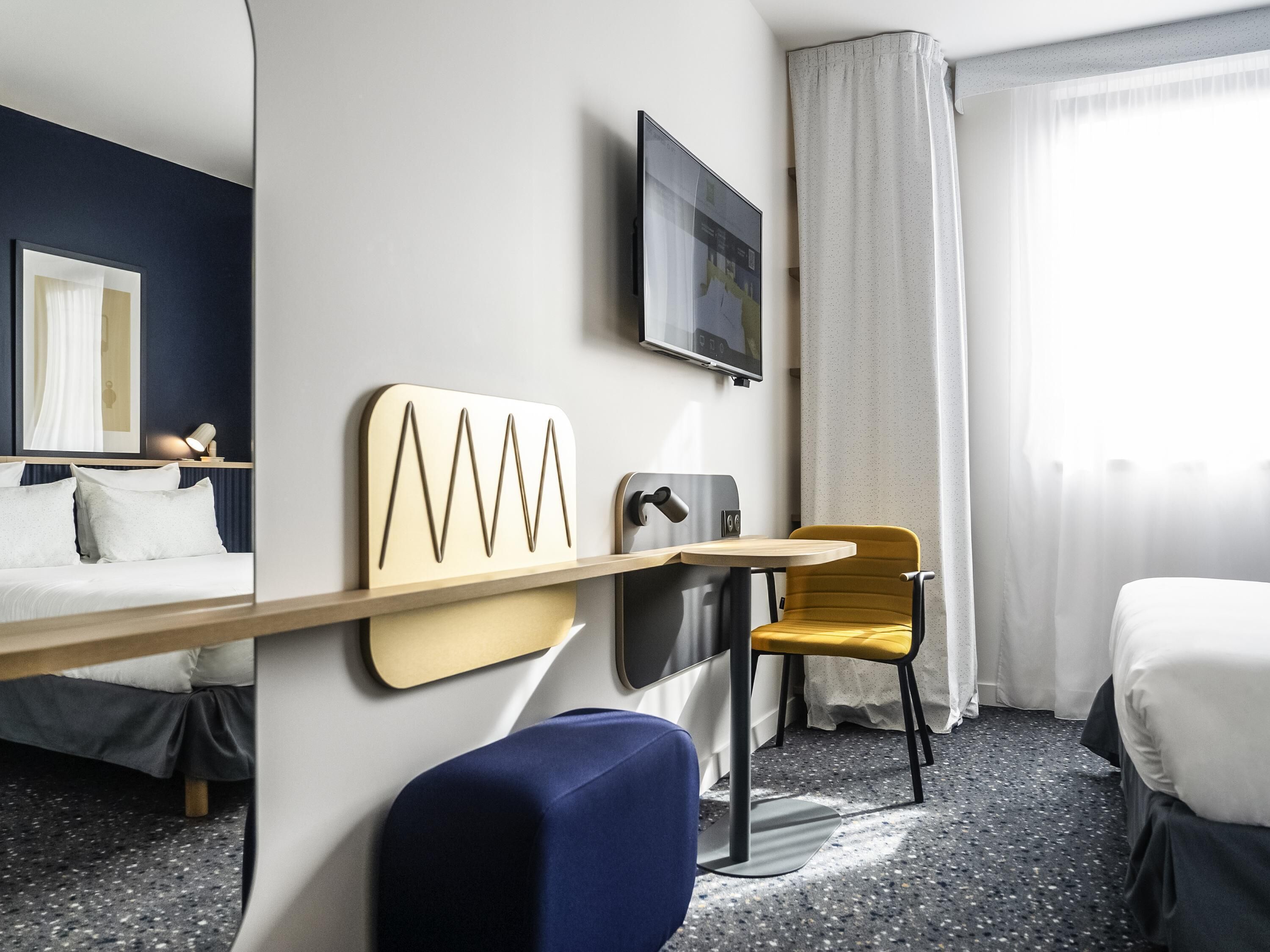 Una habitación de hotel con cama, escritorio, silla, televisión y ventana con cortinas.