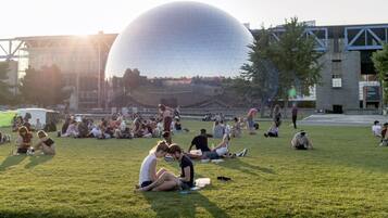 Un parc public où l’on voit des gens assis sur l’herbe, une grande structure sphérique en arrière-plan et un pont.