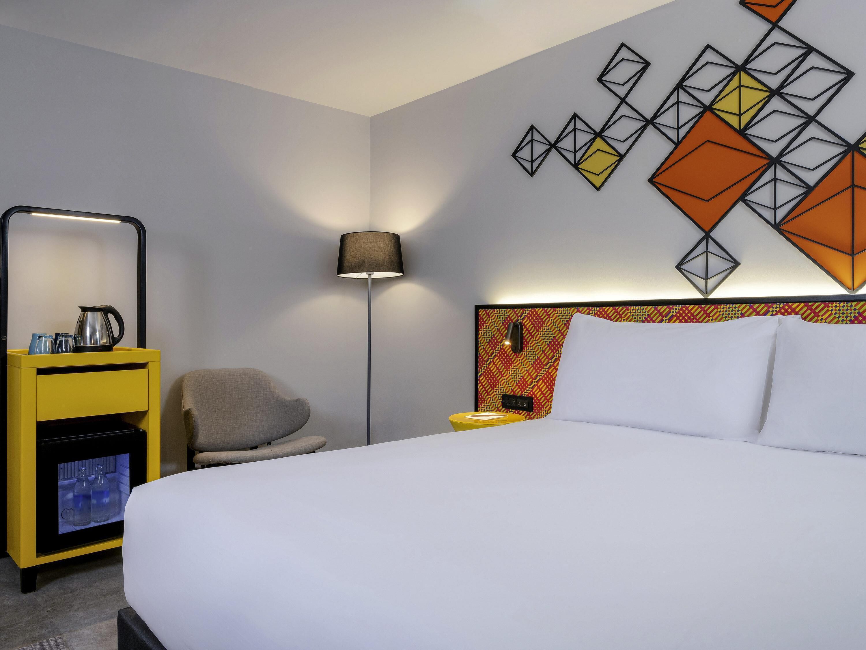 Une chambre d’hôtel comprenant un lit, une chaise, une table de chevet avec une lampe et une œuvre d’art murale.