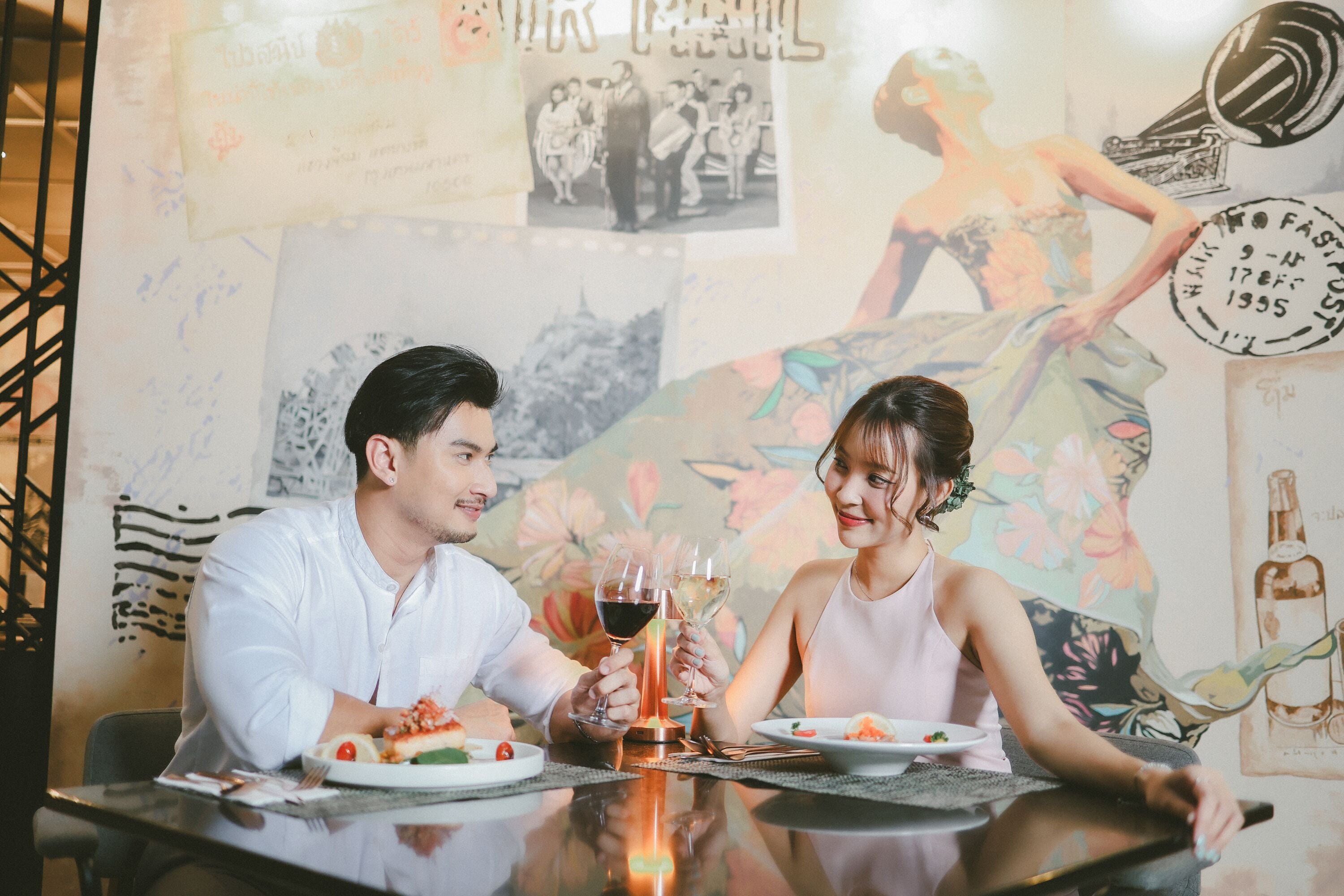 A couple dining at a table with a glass of wine, surrounded by artwork and a decorative wall.