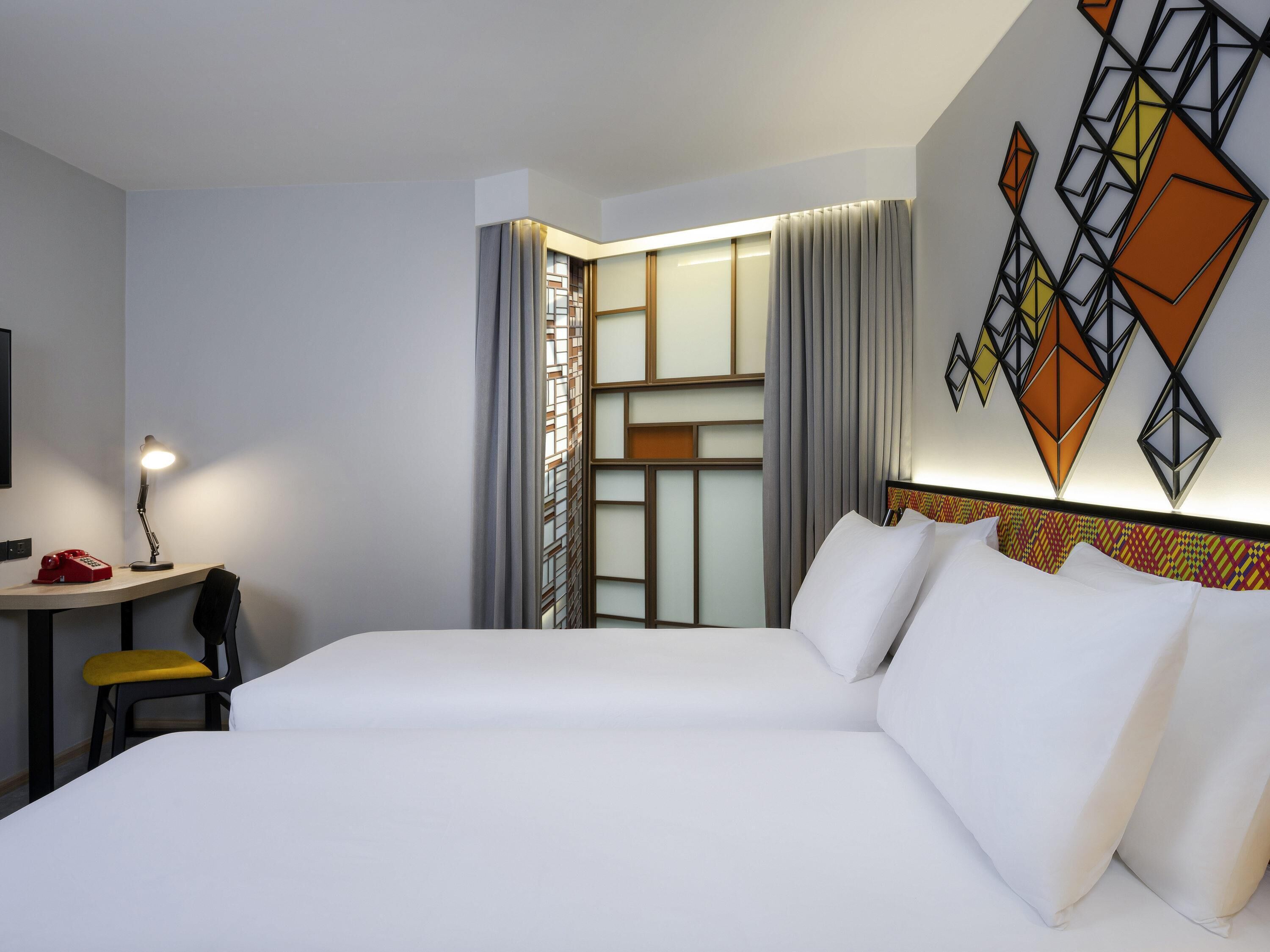 Camera d'albergo con un letto grande, una scrivania con lampada, una sedia e un pannello decorativo a parete.
