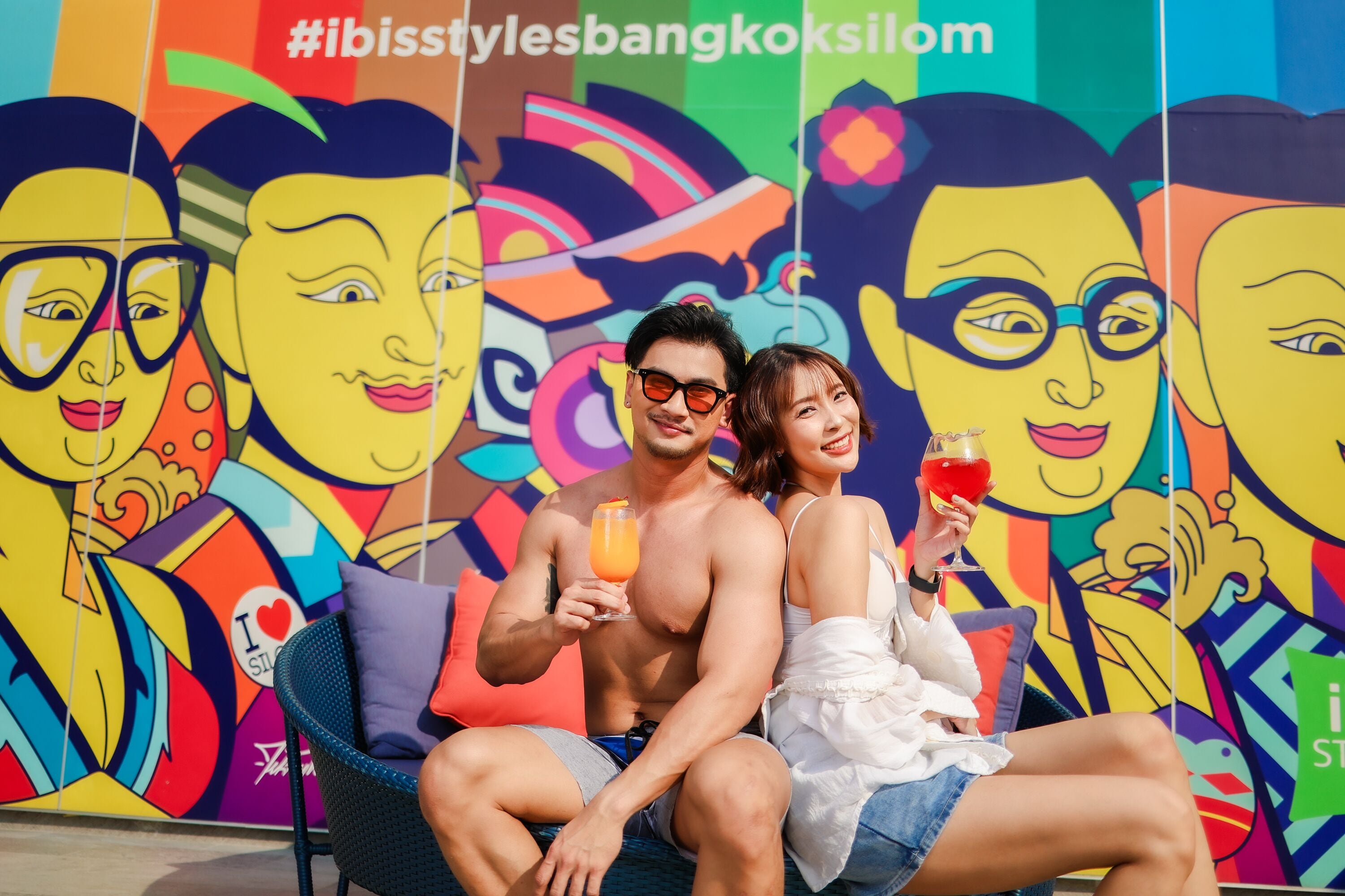 A couple sitting on a lounge chair with a colorful mural in the background.