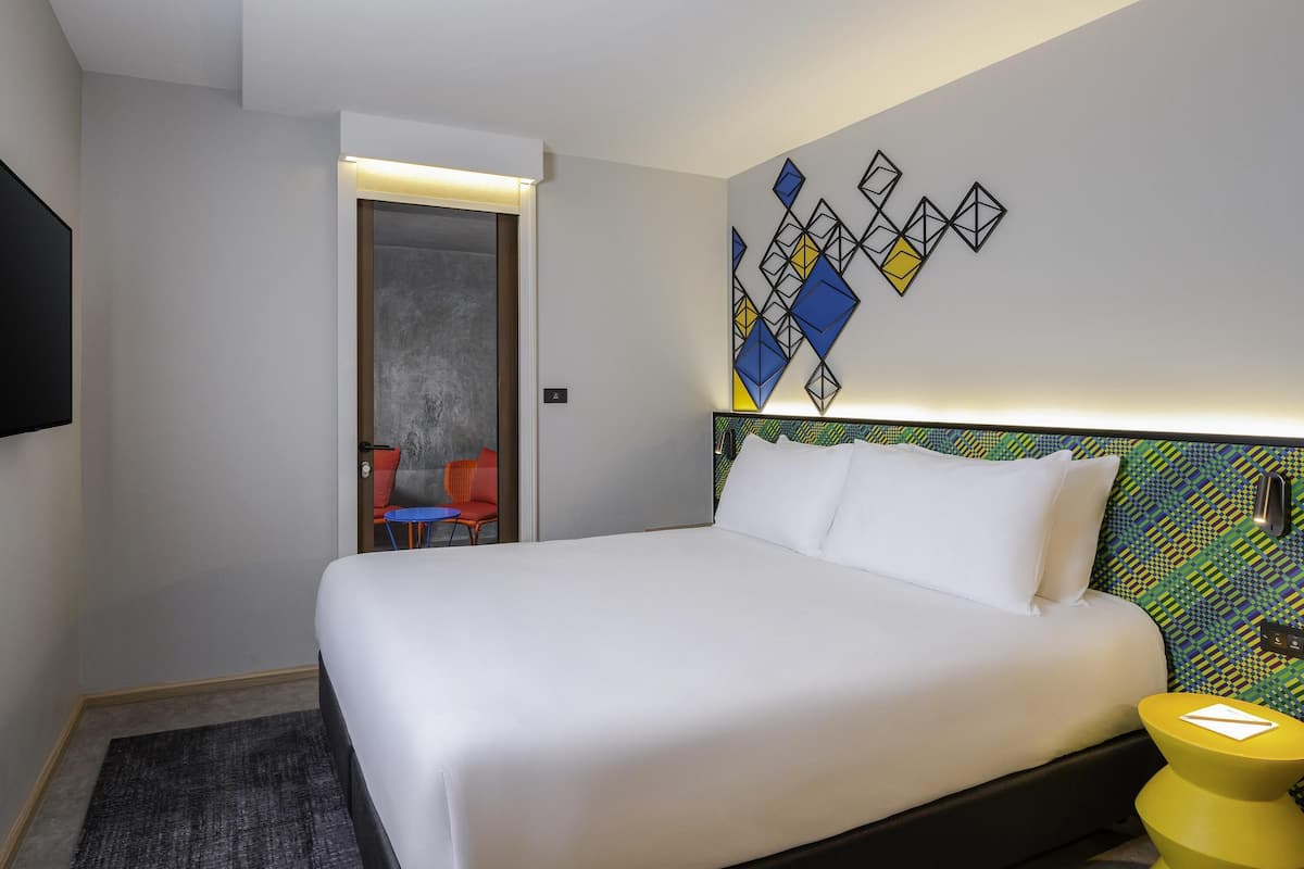 A modern hotel room with a large bed, a small table, and a chair.