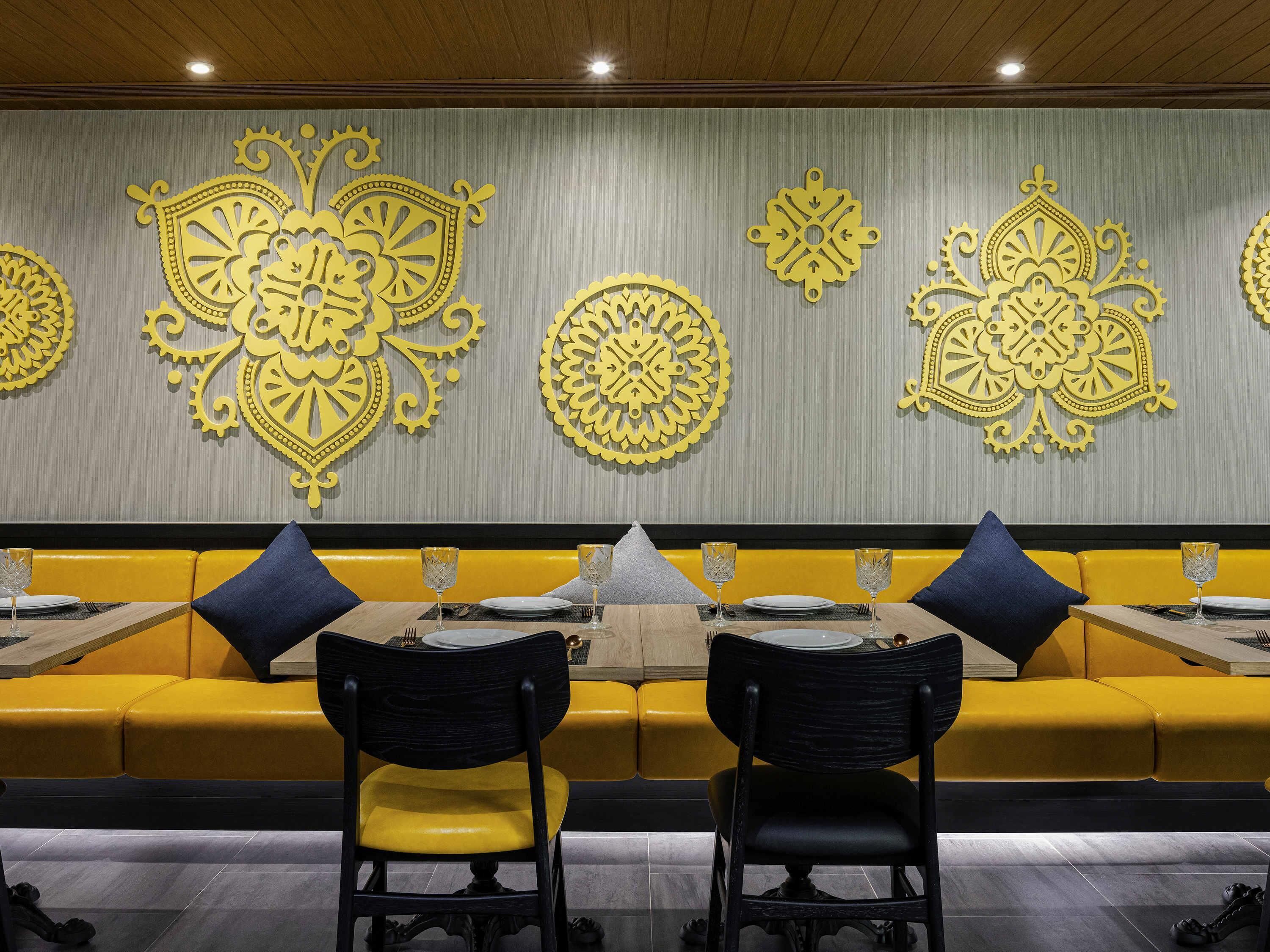 A restaurant with yellow booths and black chairs, featuring ornate wall decorations.