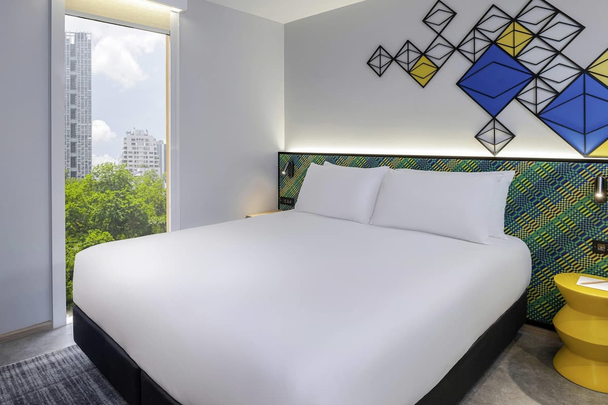 A hotel room with a bed, a view of the city, and a geometric wall art piece.