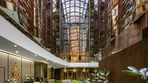 Un vestíbulo de hotel con techo alto, paredes de vidrio y una escalera central.
