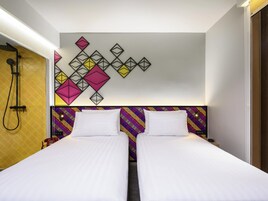 A hotel room with two beds, a colorful headboard, a geometric wall decoration, and a shower area.