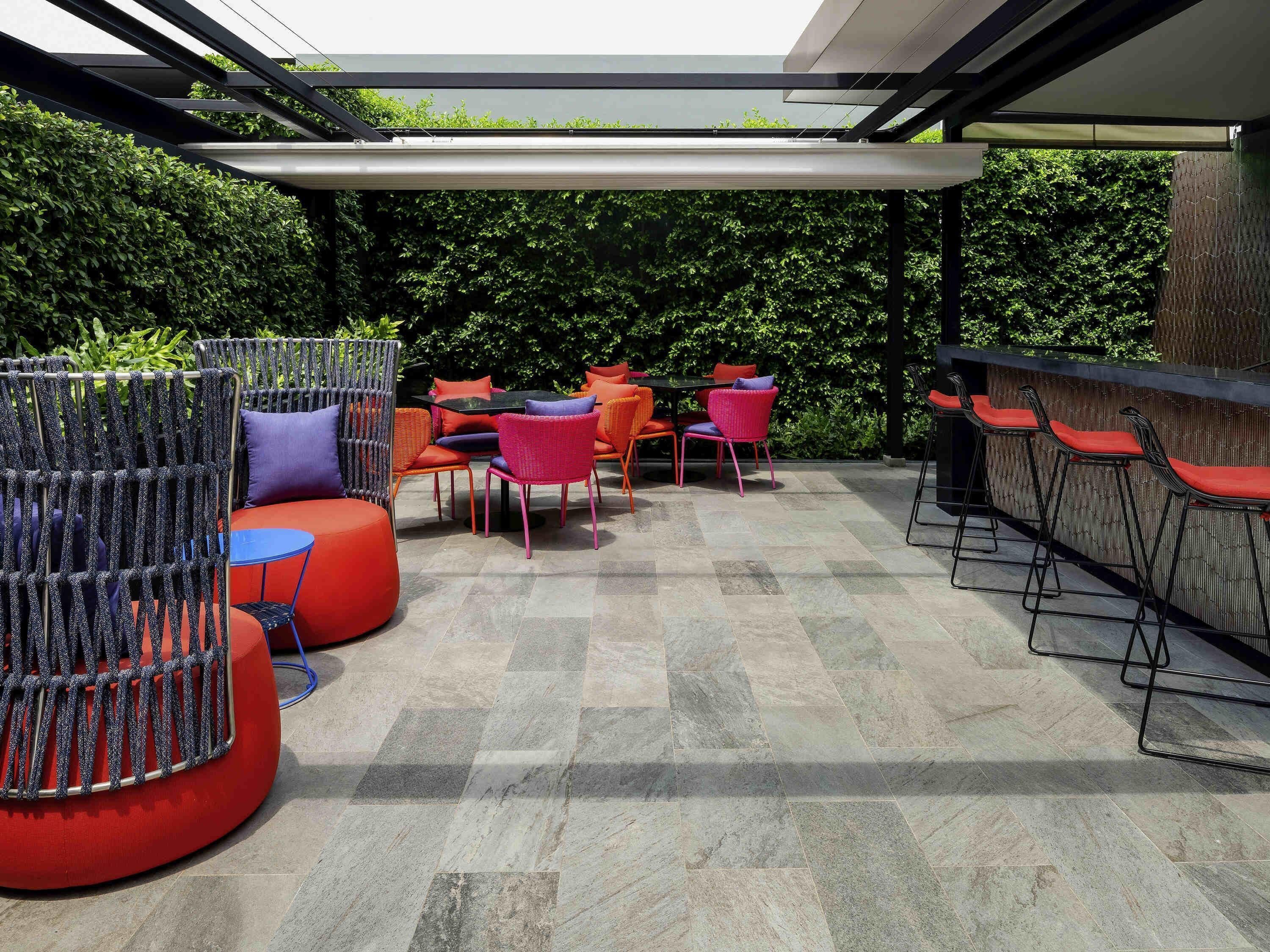 Une terrasse extérieure avec des tables et des chaises rondes, un espace salon couvert et un bar.