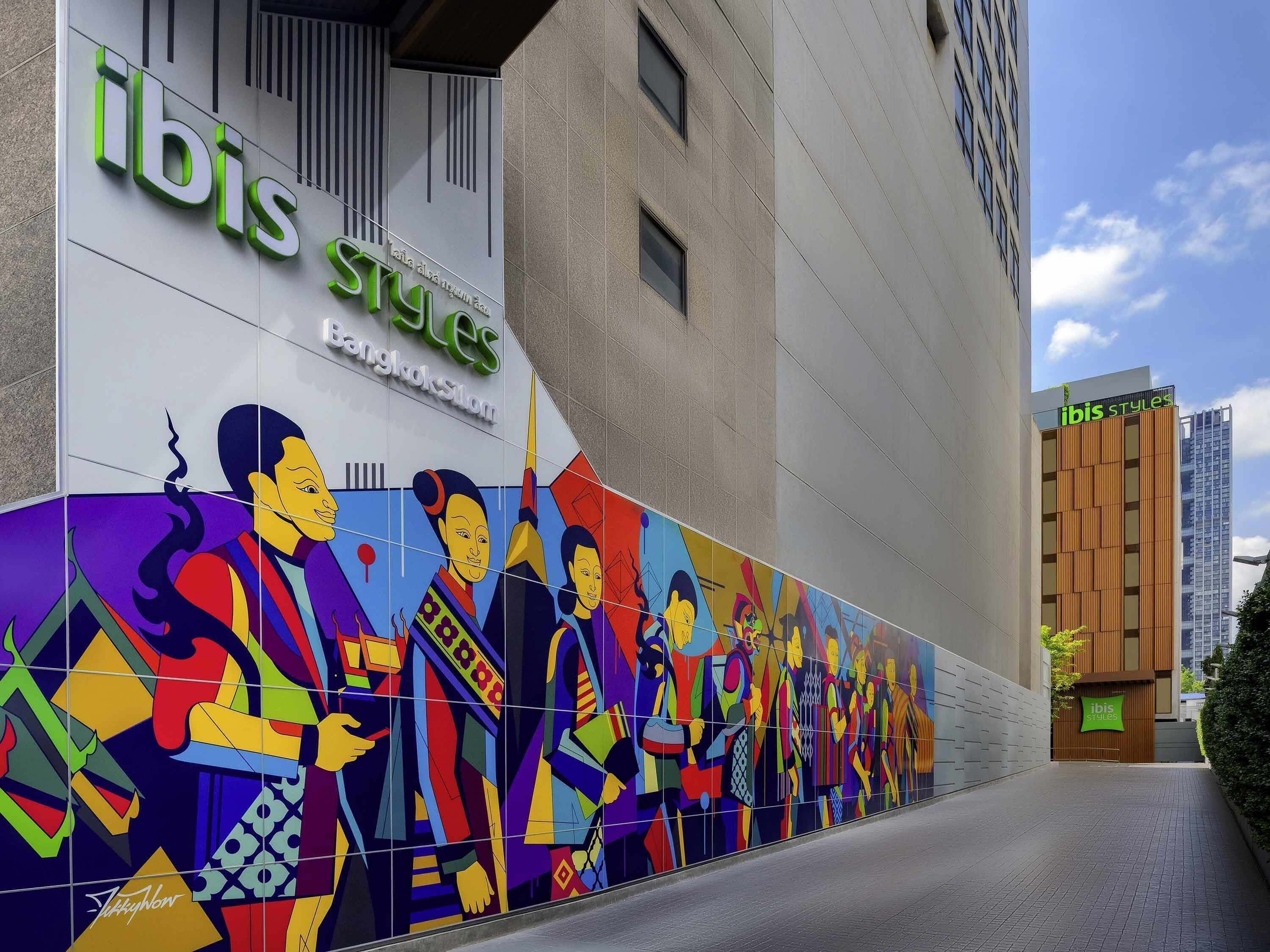 Un edificio con el letrero 'ibis Styles', un mural colorido en la fachada y un diseño arquitectónico moderno.