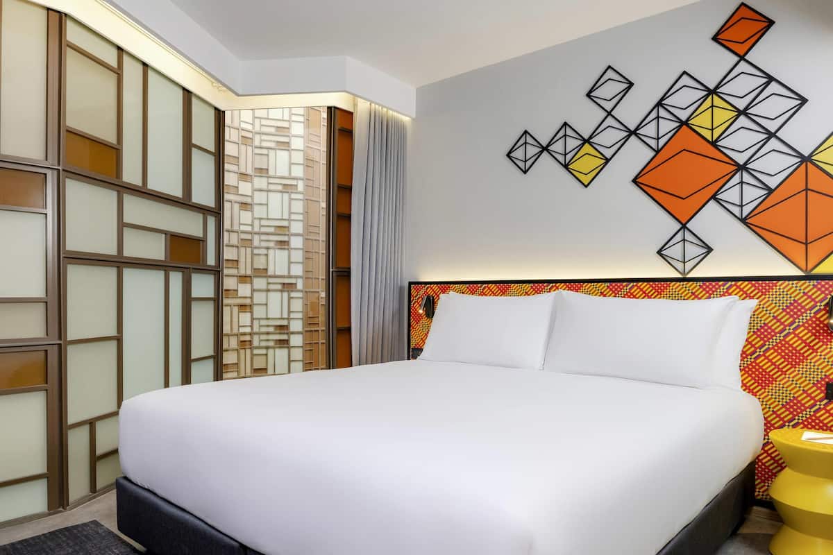 A neatly made bed in a hotel room with a geometric wall art piece above it.