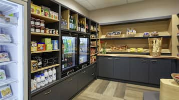 Une petite cuisine équipée d’un réfrigérateur, d’étagères remplies de provisions et d’un comptoir sur lequel se trouve un panier de pain.