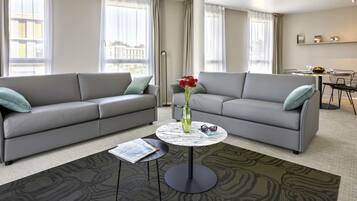 A modern living room with two grey sofas, a round coffee table, and a dining area in the background.