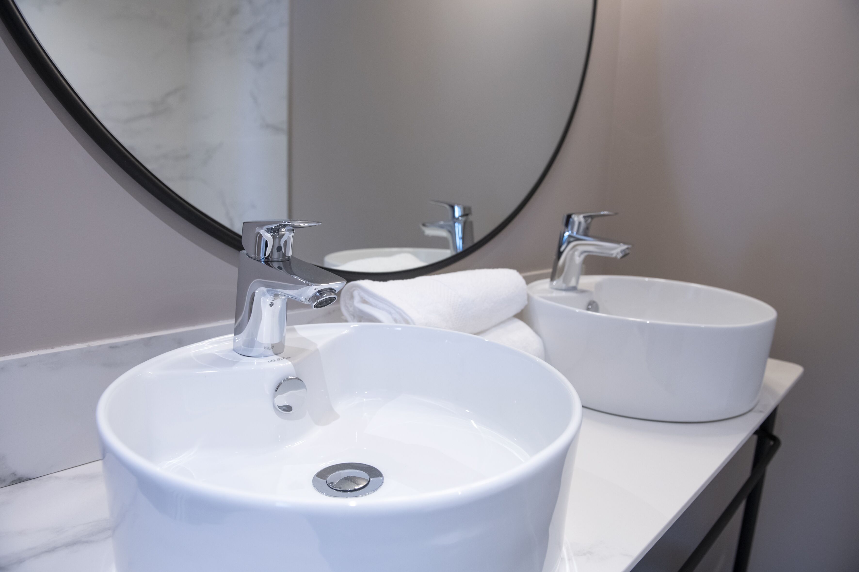 Une salle de bain avec deux lavabos blancs, un grand miroir et un comptoir en marbre.