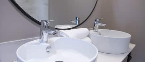 Une salle de bain avec deux lavabos blancs, un grand miroir et un comptoir en marbre.