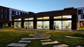 Un edificio moderno con amplios ventanales de vidrio, un camino pavimentado y un área de estar al aire libre.