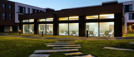A modern building with large glass windows, a paved walkway, and outdoor seating area.