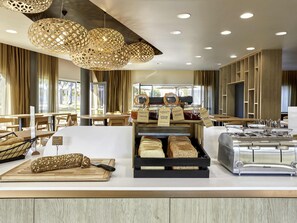 A bakery counter with bread, a cutting board, a knife, and a bread slicer. - Aparthotel Adagio & Spa Vannes (Plescop)