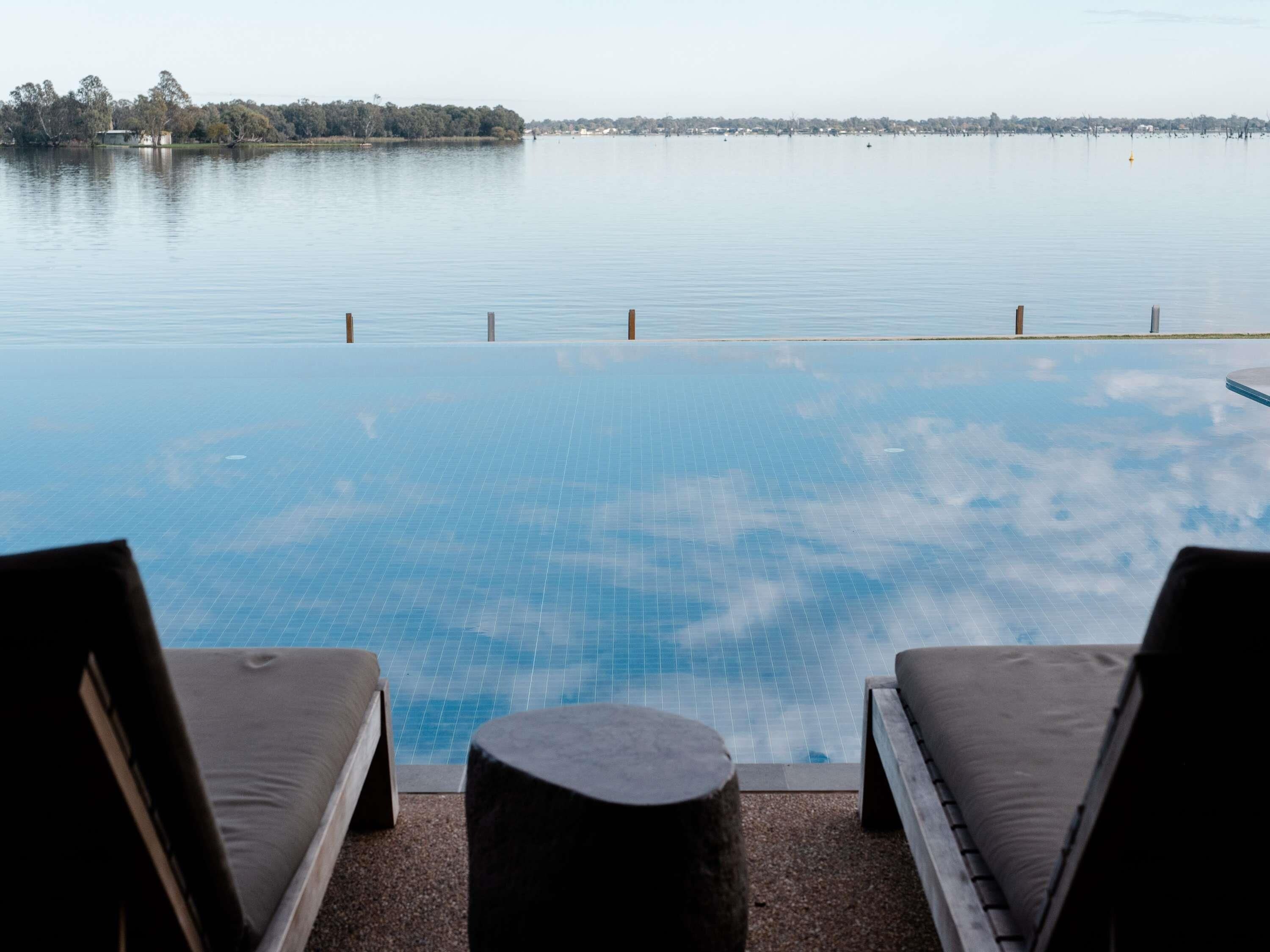 An infinity pool with a view of a calm lake and distant shoreline.