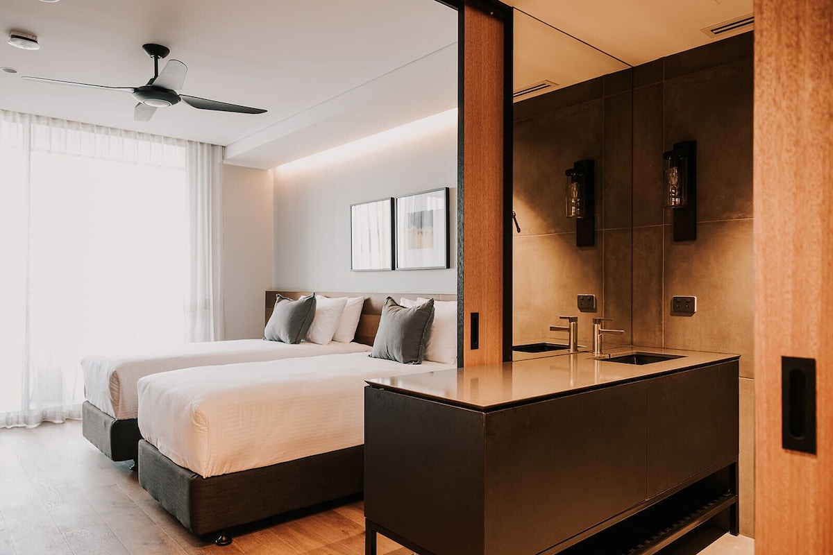 Una habitación de hotel moderna con una cama grande, tocador incorporado y ventilador de techo.