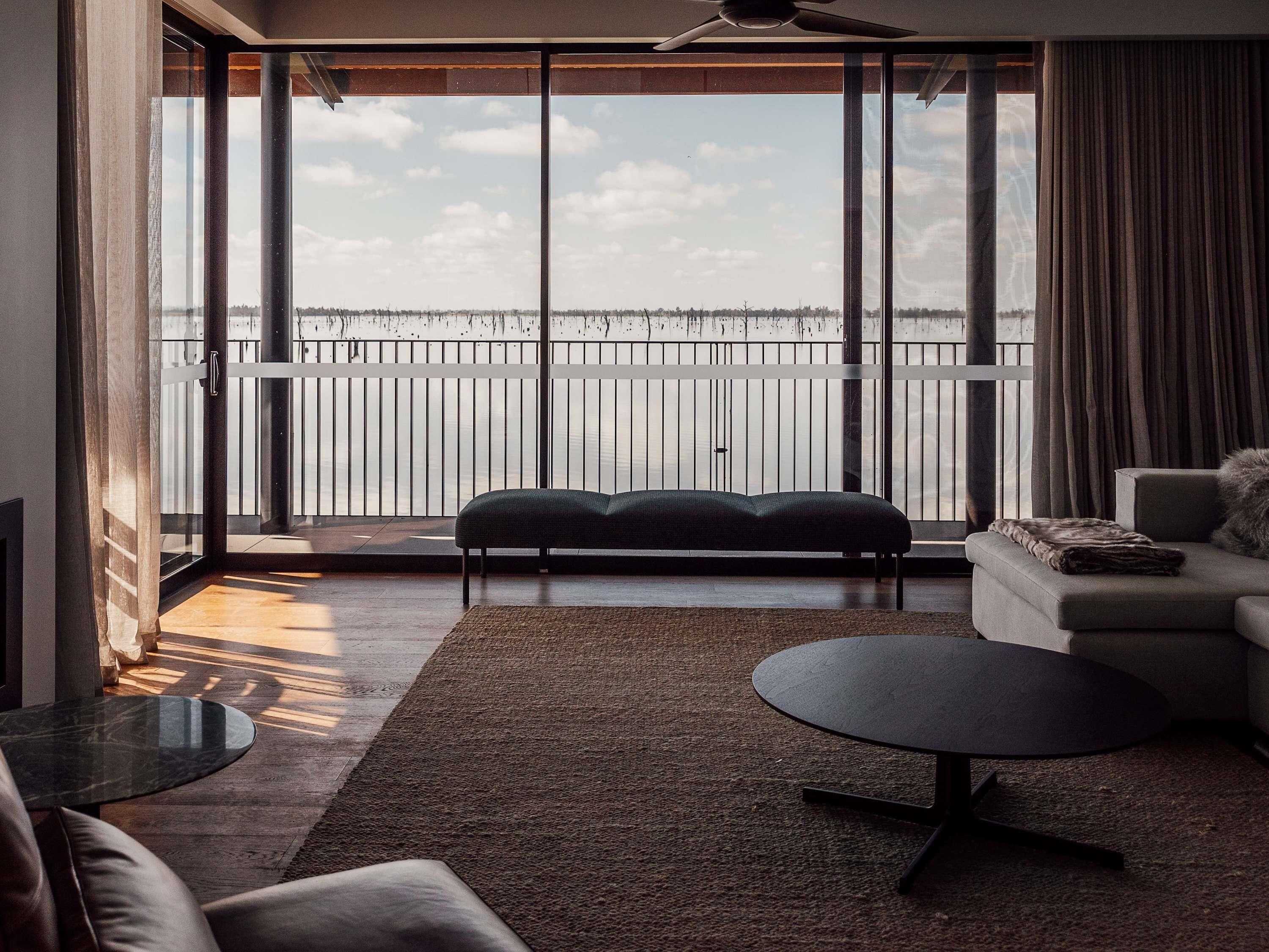 A modern living room with a large sliding glass door leading to a balcony, a sofa, a coffee table, and a view of the water.