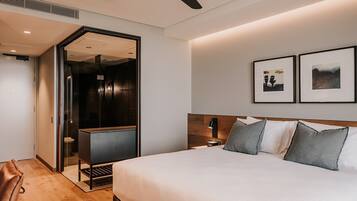 Une chambre d’hôtel moderne dotée d’un grand lit, d’une tête de lit en bois, d’une table de chevet avec une lampe et d’une porte donnant accès à une salle de bain.