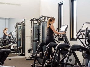 Une salle de sport équipée de tapis de course, d’appareils de musculation et d’un mur recouvert de miroirs.