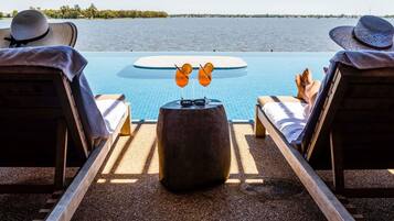 Un espace de détente au bord de la piscine, avec deux chaises longues, une table ronde sur laquelle se trouve une boisson, et une vue sur l’eau.