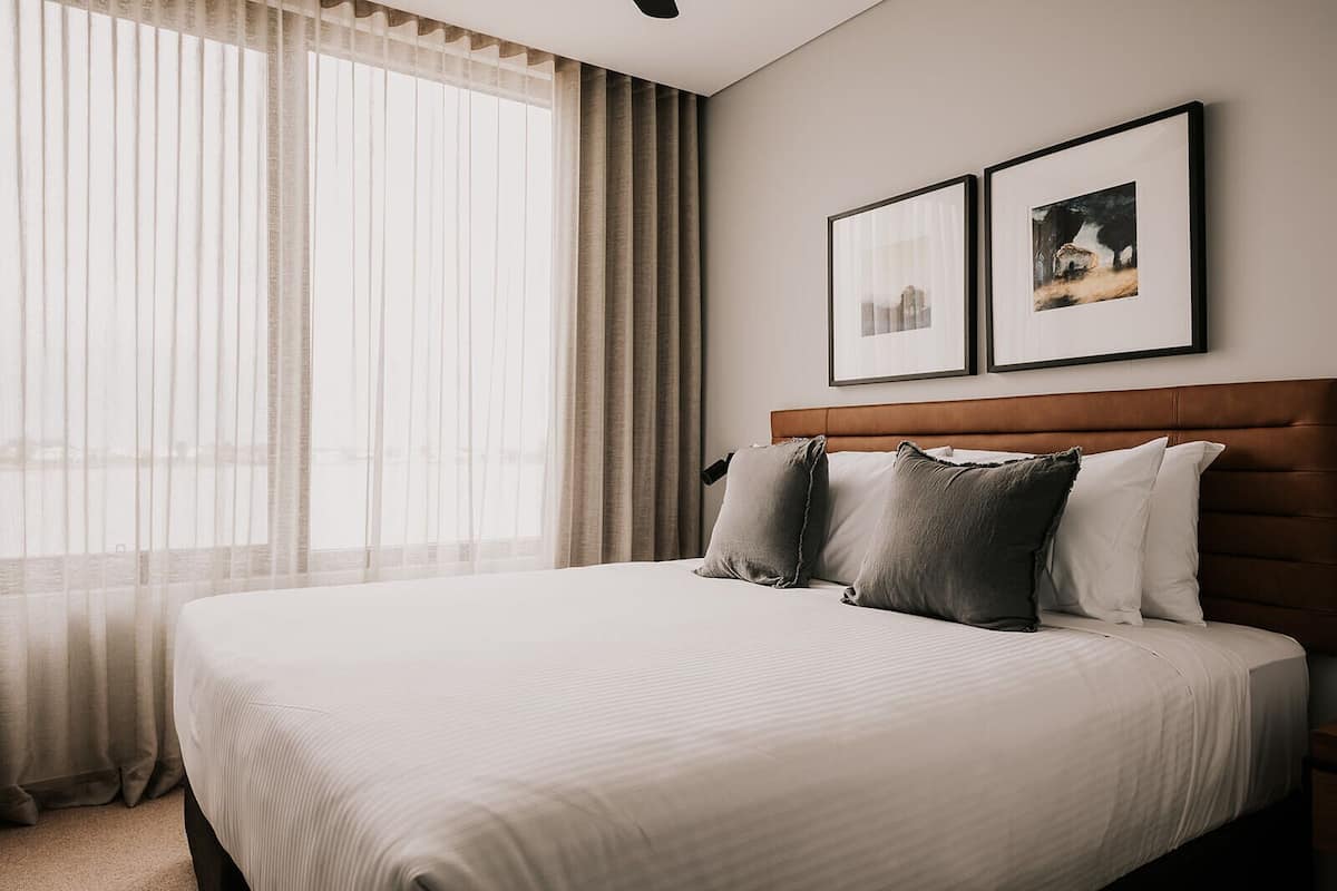 A hotel room with a large bed, a wooden headboard, and two framed pictures on the wall.