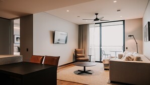 Una sala de estar moderna con comedor, sofá, sillón, televisor y balcón con vistas.