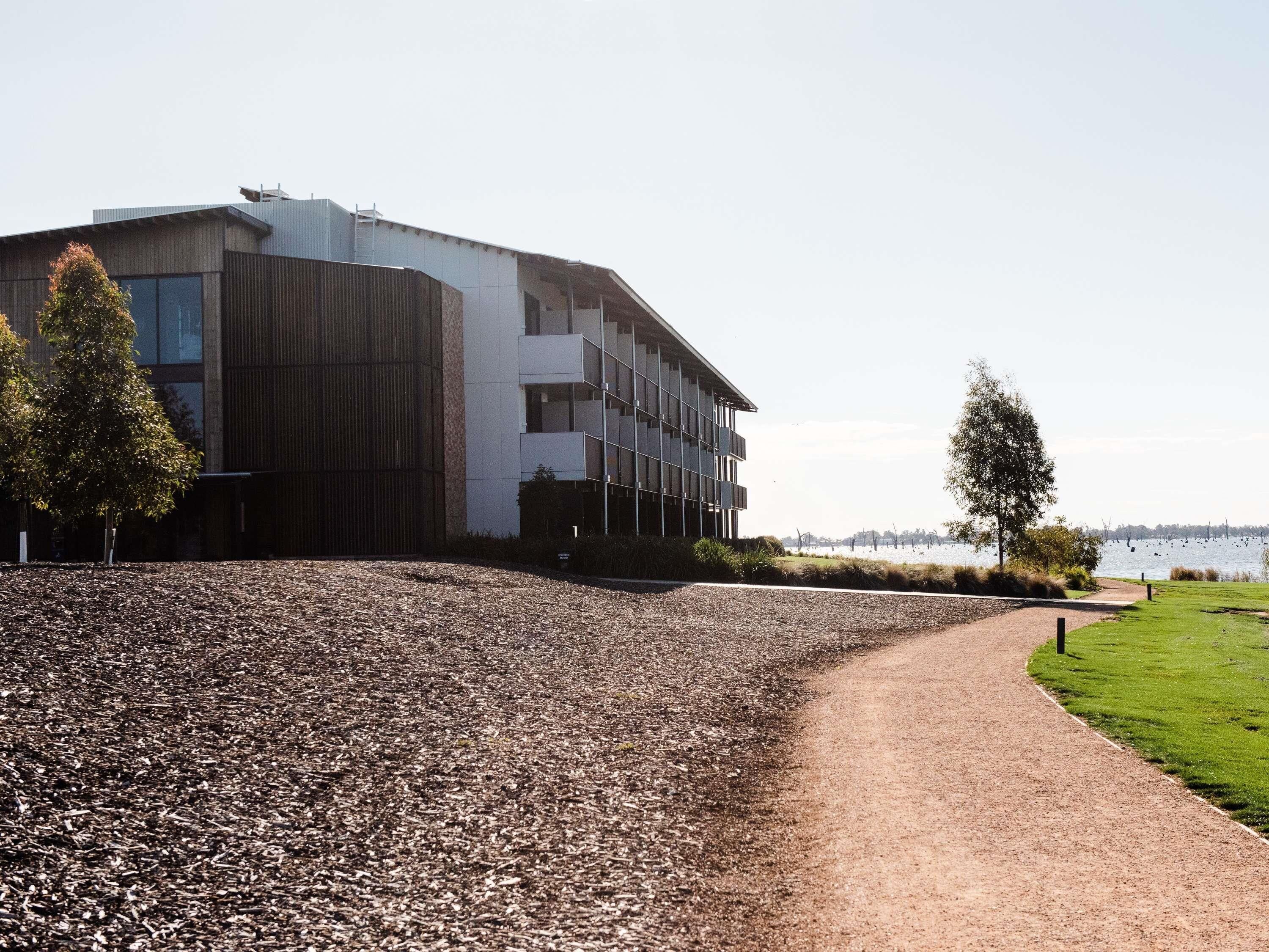 A modern building with a gravel path leading to a grassy area by a body of water.