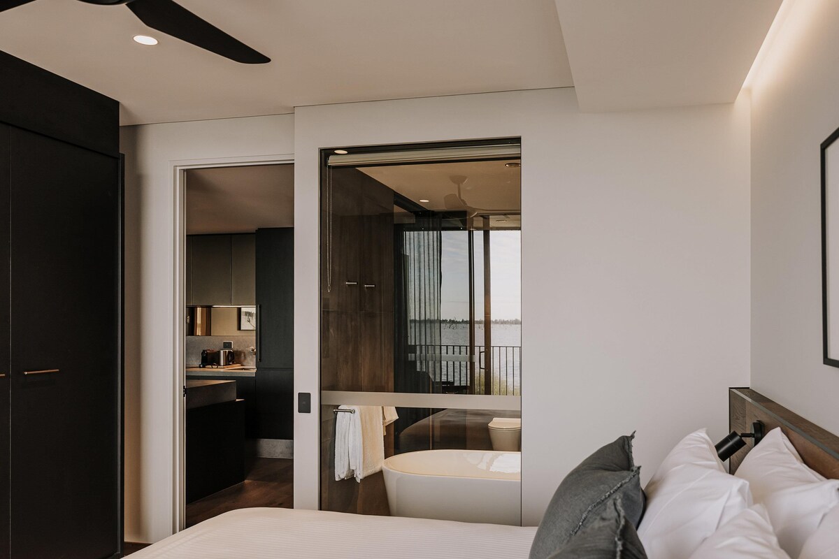 Una habitación de hotel moderna con cama, baño, kitchenette y balcón con vistas.