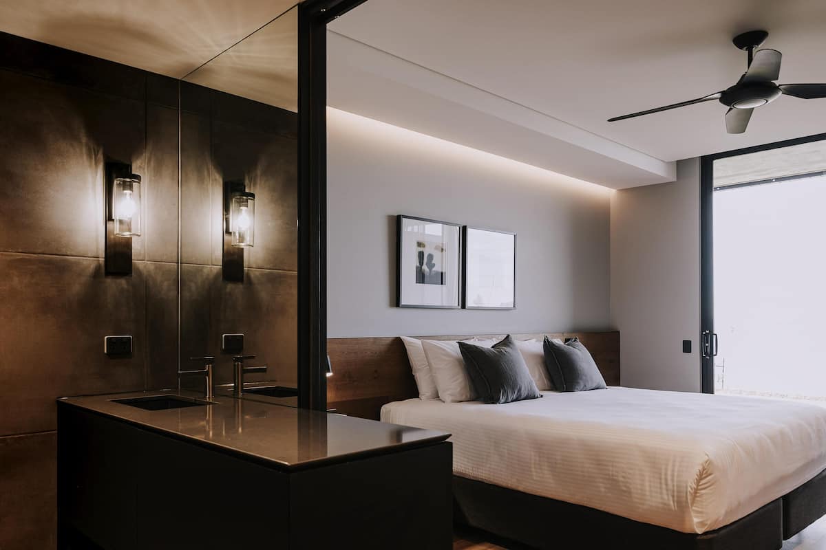 A modern bedroom with a large bed, a bedside table, a built-in bench, and a ceiling fan.
