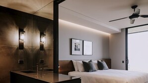 Habitación de hotel moderna con una cama grande, una mesita de noche, tocador empotrado con espejo e iluminación en la pared.