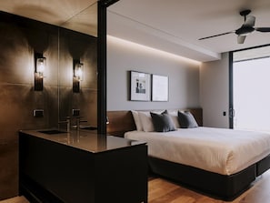 A modern hotel room with a large bed, a bedside table, a built-in vanity with a mirror, and wall-mounted lights.