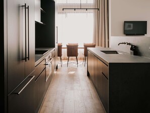 A modern kitchen with stainless steel appliances, a dining area with two chairs, and a large window providing natural light. - The Sebel Yarrawonga Silverwoods (Yarrawonga)