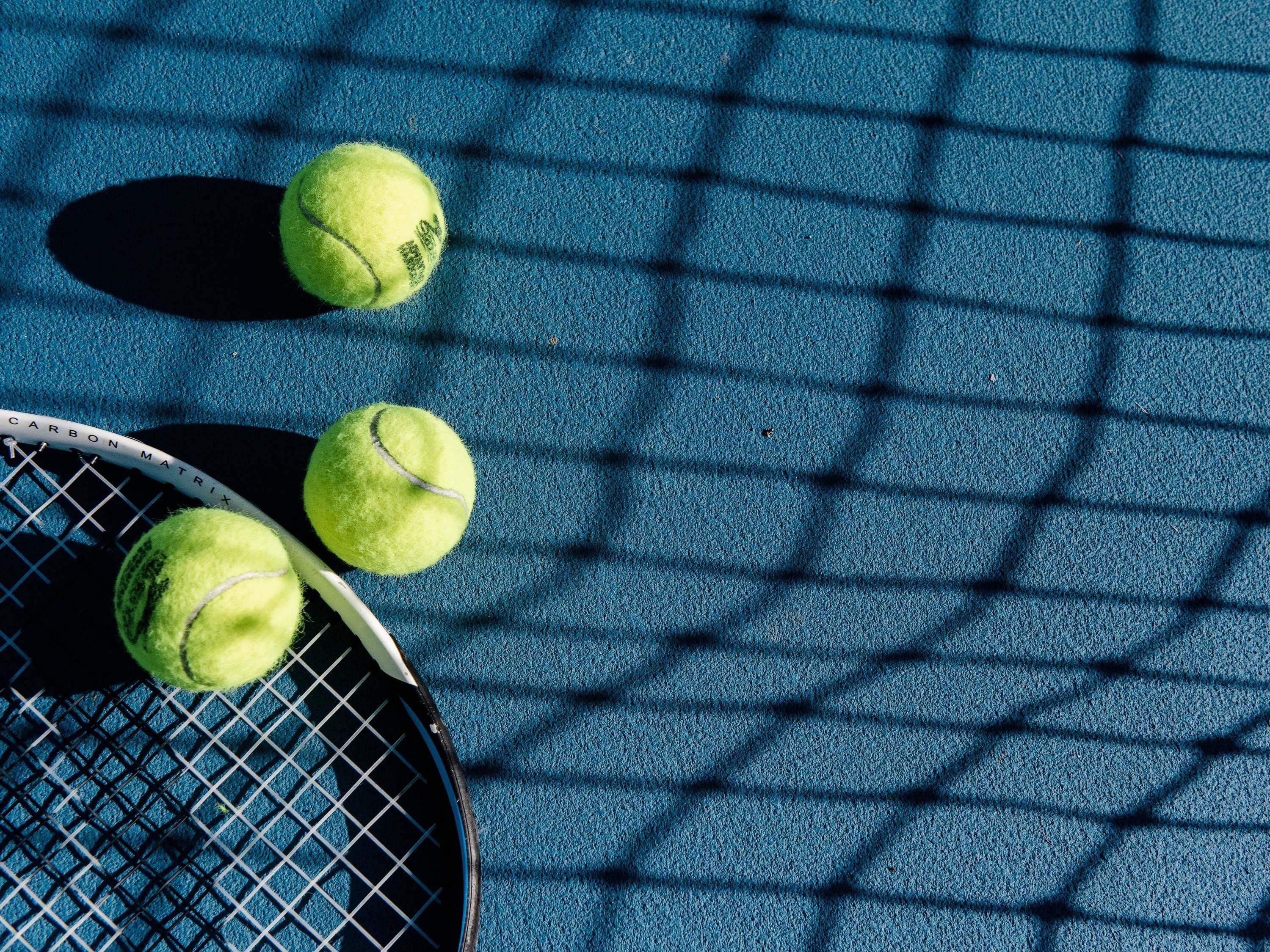 Una raqueta de tenis y tres pelotas de tenis sobre una superficie azul con textura.