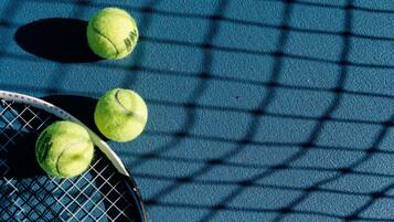 Una raqueta de tenis y tres pelotas de tenis sobre una superficie azul con textura.