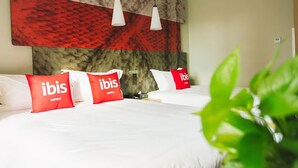 Une chambre d’hôtel avec deux lits, des oreillers rouges à l’effigie d’« ibis », une tête de lit en marbre et des lampes suspendues.