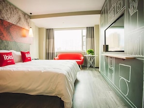 A hotel room with a bed, red pillows, a red chair, a small table with a plant, and a TV mounted on the wall. - Ibis Lanzhou Xigu Yumen Street Hotel (Lanzhou)