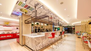 Een modern café met een lange toonbank, rode stoelen en een plafond met artistieke decoraties.