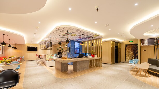 Een moderne hotellobby met een receptiebalie, een zithoek en een groot scherm dat informatie toont.