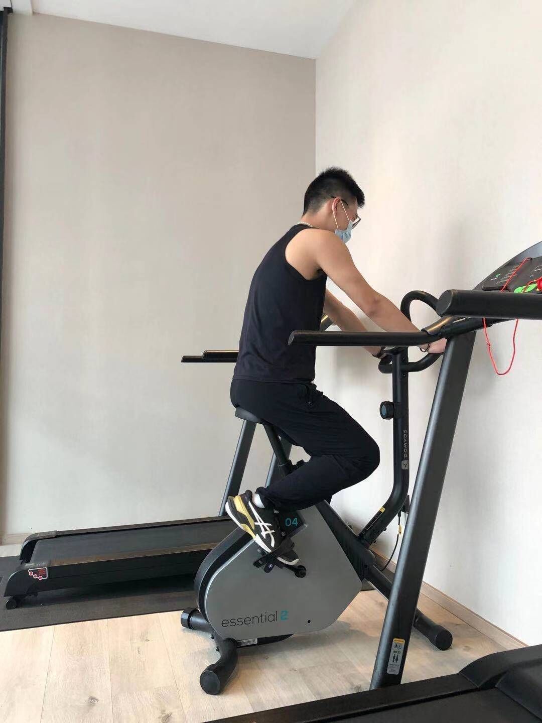 A person using a stationary bike in a room with a wooden floor and a plain wall.