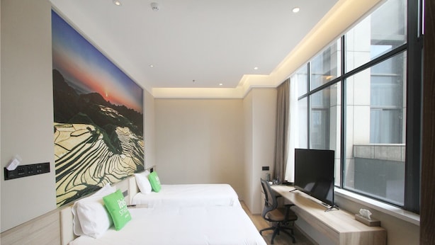 Une chambre d’hôtel moderne avec deux lits, un bureau équipé d’un ordinateur, une grande fenêtre et un tableau au mur.
