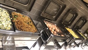 Un buffet proposant une variété de plats, notamment des nouilles, du riz, des œufs et des légumes.