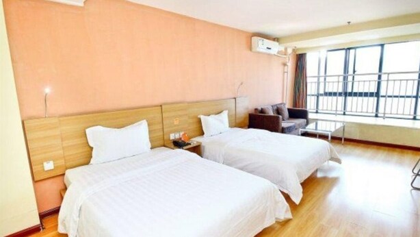 Habitación de hotel con dos camas, piso de madera, ventana con vistas y una pequeña mesa con una silla.