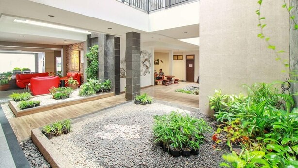 A spacious indoor area with a central garden, seating areas, and a staircase leading to an upper level. - Collection O Sweet Karina (Bandung)