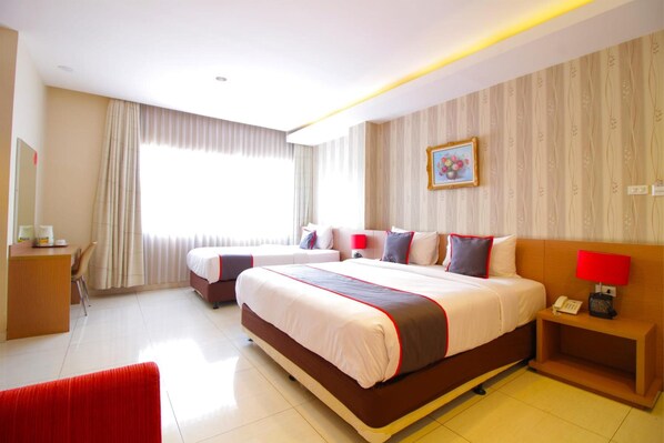 A hotel room with two beds, a desk, a chair, a red sofa, a nightstand with a lamp, and a framed picture on the wall. - Collection O Sweet Karina (Bandung)